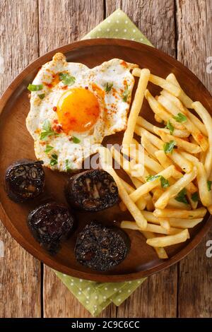 Huevos rotos con morcilla œuf frit avec frites et saucisse de sang dans une assiette sur la table. Vue verticale du dessus Banque D'Images