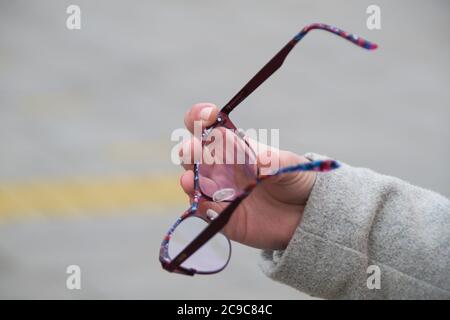 Gros plan de la main d'une femme tenant des lunettes de lecture dans une rue. Espace négatif. Espace de copie pour la publicité. Banque D'Images