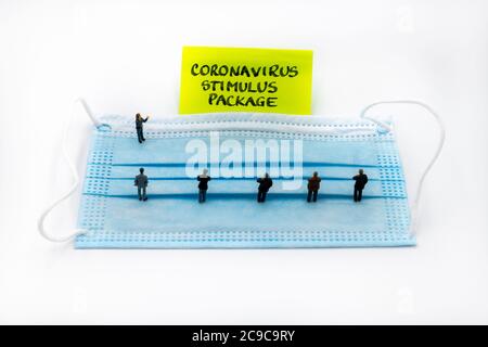 Figurines miniatures posées comme des gens d'affaires se tenant socialement distancé sur le masque médical lors d'une réunion regardant la note post-it avec le coronavirus Banque D'Images