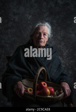 Femme aux cheveux gris portant un châle tenant un panier de pommes Banque D'Images