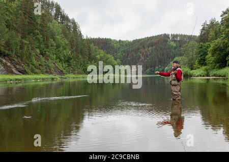 pêcheur âgé utilisant la canne de pêche dans la rivière de montagne en tissu imperméable Banque D'Images