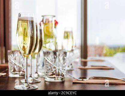 Table posée avec quatre verres de champagne et carafe, et des verres de limonade en cristal sur fond de bokeh. Banque D'Images