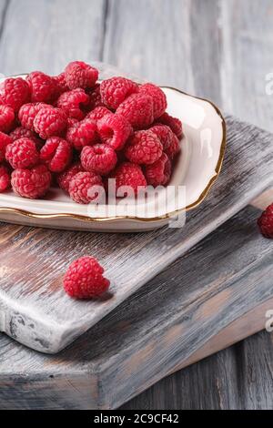 Fruits à la framboise dans une assiette sur de vieilles planches à découper, pile saine de baies d'été sur fond de bois gris, vue en angle macro Banque D'Images