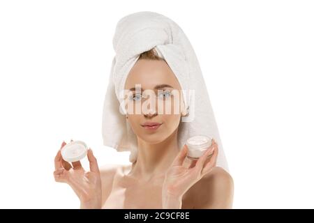 Journée beauté. Jeune femme caucasienne portant une serviette faisant sa routine quotidienne de soin de la peau avec hydratant. Portrait sur fond blanc de studio. Concept de beauté, d'auto-soins, de cosmétiques, de jeunes, de week-end à la maison, de spa. Banque D'Images