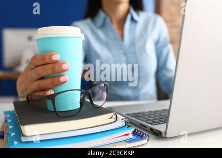 La main féminine tient le verre bleu avec le café sur le lieu de travail. Banque D'Images