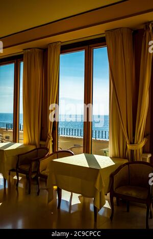 Les tables d'un hôtel avec une vue splendide sur la mer de la fenêtre. La lumière entre par la fenêtre le jour de l'été. Vacances, détente, luxe, Banque D'Images