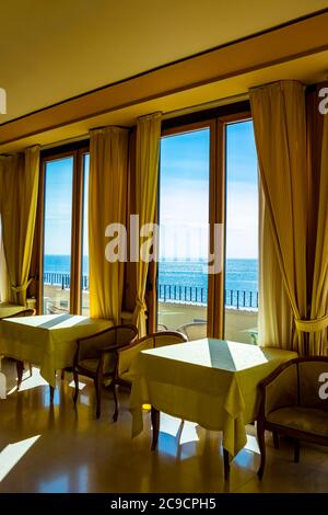 Les tables d'un hôtel avec une vue splendide sur la mer de la fenêtre. La lumière entre par la fenêtre le jour de l'été. Vacances, détente, luxe, Banque D'Images