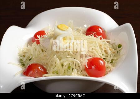 Salade délicieuse servie au restaurant, avec légumes, poulet et pain frit, saupoudrée de fromage et décorée de tomates cerises et de caille Banque D'Images