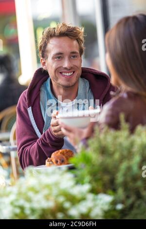 Homme parlant avec une petite amie à la table du café. Rencontre d'amis en ville pour boire un café amusant. Couple à une date, jeunes ayant un brunch à Banque D'Images