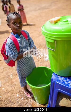 Une jeune fille se lave les mains à un poste de lavage des mains de son école à Conakry, Guinée, Afrique de l'Ouest. Banque D'Images