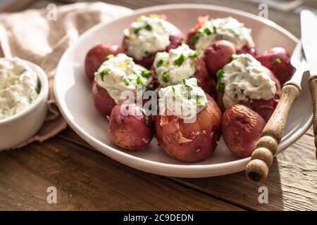 Jeunes pommes de terre bouillies à la crème sure et à l'oignon vert sur fond de bois Banque D'Images