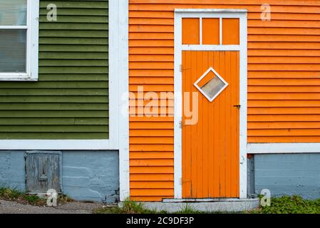 Une porte extérieure en bois orange avec une fenêtre en forme de losange dans un bâtiment à panneaux de bois orange et vert. Banque D'Images