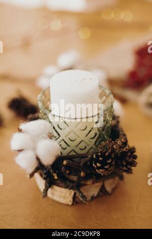 Bougie de Noël dans un support rustique en branches, coton, anis et cônes de pin sur une table en bois avec des lumières festives. Atelier de vacances. Fabrication rustique Banque D'Images