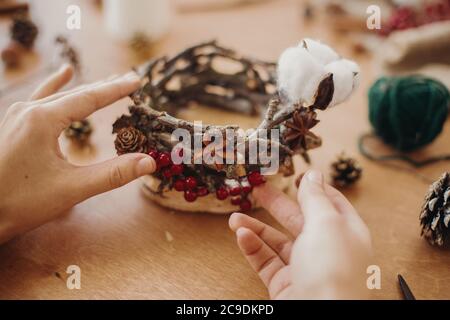 Fleuriste faisant rustique bougie de noël porte-bougie. Mains tenant des cônes de pin, des branches, anis et faisant rustique décoration festive sur table en bois. Vacances Banque D'Images