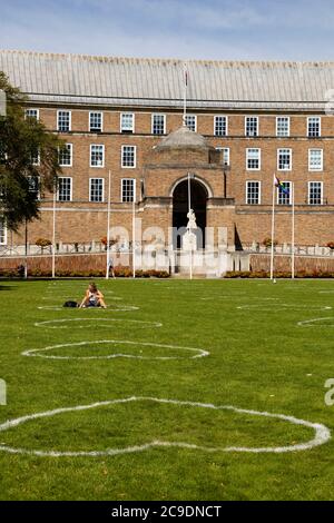 Fille assise à Loveheart peint sur l'herbe indiquant 2 mètres de distance de sécurité à College Green, avec l'hôtel de ville, pendant la pandémie Covid 19, BRI Banque D'Images