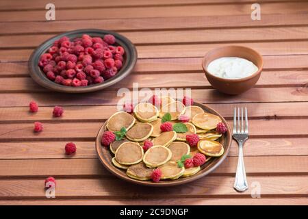 Céréales pancakes et framboises fraîches mûres rouges dans une assiette brune sur une table en bois. Délicieux petit déjeuner d'été Banque D'Images