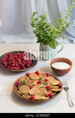 Céréales pancakes et framboises fraîches mûres dans une assiette brune sur une table en bois blanc près de la fenêtre. Délicieux petit déjeuner d'été Banque D'Images