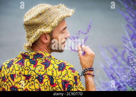 bel homme barbu avec chapeau de paille en plein air qui sent les fleurs violettes Banque D'Images