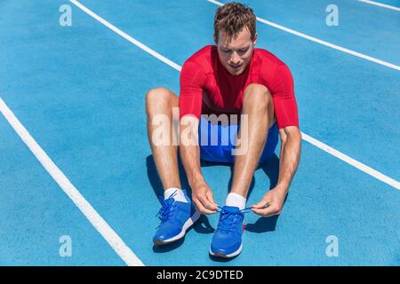 Athlète sprinter se prépare à courir attacher les lacets de chaussures sur les pistes de course du stade. Homme coureur se préparant pour l'entraînement cardio en plein air. Fitness et Banque D'Images