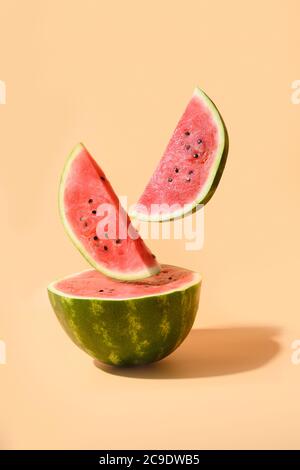 Melon d'eau tranché volant sous fond de papier beige. Composition verticale. Banque D'Images