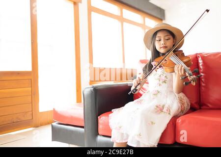 Une mignonne fille d'école élémentaire asiatique joue un violon heureusement dans sa maison. Banque D'Images