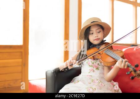 Une mignonne fille d'école élémentaire asiatique joue un violon heureusement dans sa maison. Banque D'Images