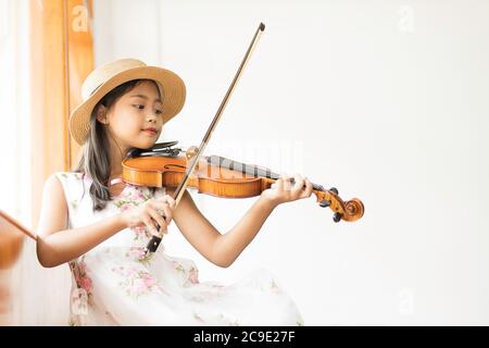 Une mignonne fille d'école élémentaire asiatique joue un violon heureusement dans sa maison. Banque D'Images