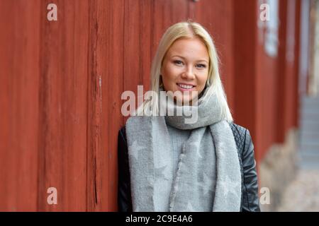 Bonne jeune belle femme blonde penchée contre un mur en bois rouge Banque D'Images