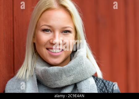 Bonne jeune belle femme blonde penchée contre un mur en bois rouge Banque D'Images