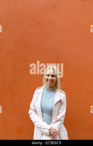 Bonne jeune belle femme blonde souriante contre le mur orange Banque D'Images