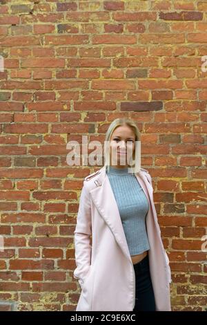 Jeune belle femme blonde debout contre le mur de brique Banque D'Images