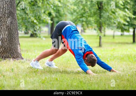 L'homme pratique le yoga dans le parc. L'homme adulte fait face au chien posé sur une herbe verte dans le parc public. Banque D'Images