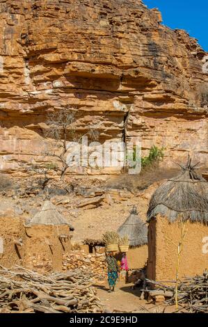 Une femme portant un panier avec millet sur sa tête dans le village Dogon de Songho dans l'escarpement de Bandiagara (site du patrimoine mondial de l'UNESCO) dans le Dogo Banque D'Images