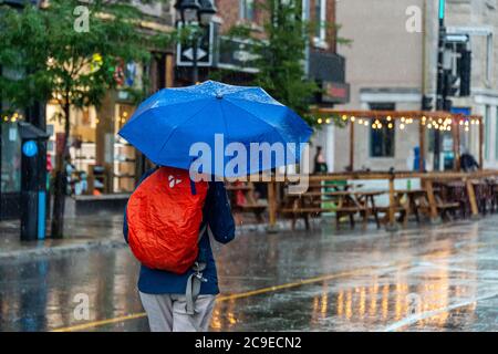 Montréal, CA - 30 juillet 2020 : femme sur l'avenue Mont-Royal tenant un parapluie sous la pluie et la tempête Banque D'Images