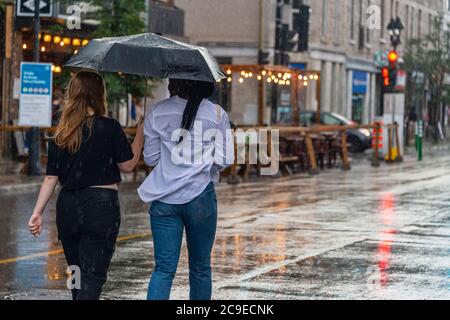 Montréal, CA - 30 juillet 2020 : personnes sur l'avenue Mont-Royal tenant un parapluie sous la pluie et la tempête Banque D'Images