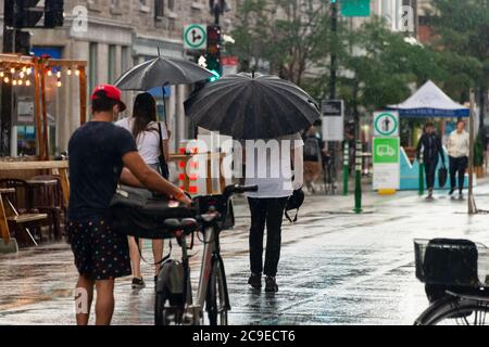 Montréal, CA - 30 juillet 2020 : personnes sur l'avenue Mont-Royal tenant des parasols sous la pluie et la tempête Banque D'Images