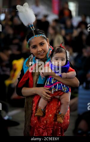 San Francisco, États-Unis - 08 février 2020 : jeune femme amérindienne ou indienne vêtue d'une tenue traditionnelle colorée tenant une petite fille sous le coup d'un pow-wow Banque D'Images