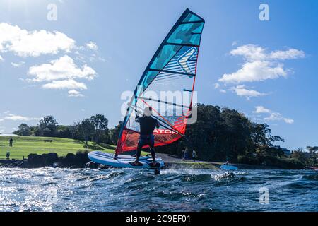 Un jeune homme en combinaison navigue sur un lac une planche à voile hydrofoil. Fond bleu ciel. Banque D'Images