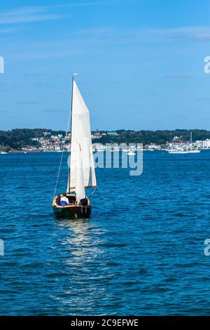 Quelques personnes sont sur un petit bateau en bois naviguant des voiles complètes devant. C'est un après-midi ensoleillé et la mer est calme. Il y a une bannière blanche sur le dessus du mât Banque D'Images