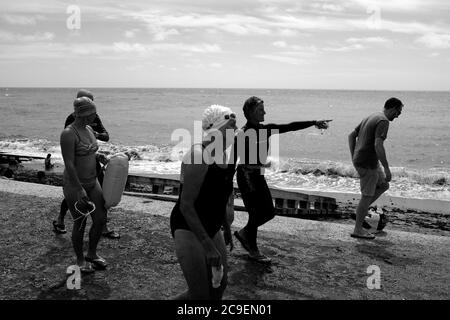 Un groupe de nageurs dans leurs costumes de natation marchant le long du front de mer à Freshwater Bay sur l'île de Wight. Banque D'Images