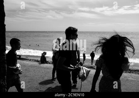 Les gens de plage se promènant le long du mur de la mer de la nouvelle-veillée entièrement habillée à Freshwater Bay sur l'île de Wight. Banque D'Images