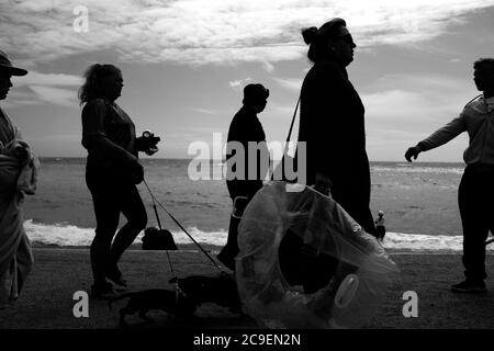 Les amateurs de plage se promènent le long du mur de la mer en silhouette habillée en marchant les chiens à Freshwater Bay sur l'île de Wight. Banque D'Images