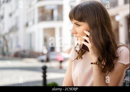 jeune fille aux cheveux longs, se tient dans la rue et parle au téléphone. La fille ne regarde pas l'appareil photo Banque D'Images