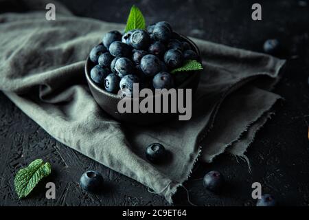 Bleuets biologiques juteux et feuilles de menthe fraîche dans le bol en céramique sombre, sur le panneau en bois noir. Banque D'Images