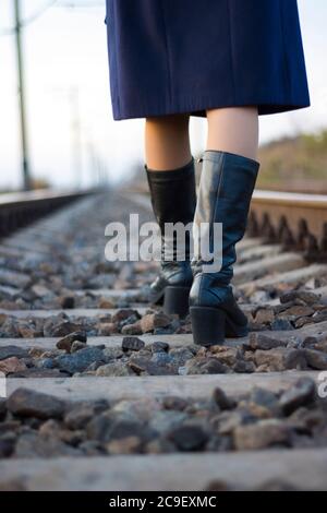 Une fille marche sur des rails de chemin de fer dans un manteau et des bottes - Voyage, dépression, style de vie Banque D'Images