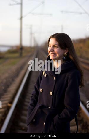 Une fille marche sur des rails de chemin de fer dans un manteau - voyage, dépression, style de vie Banque D'Images