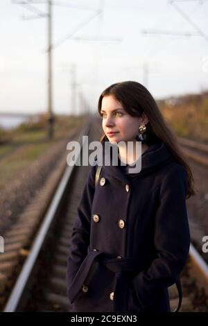 Une fille marche sur des rails de chemin de fer dans un manteau - voyage, dépression, style de vie Banque D'Images