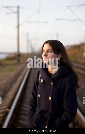 Une fille marche sur des rails de chemin de fer dans un manteau - voyage, dépression, style de vie Banque D'Images