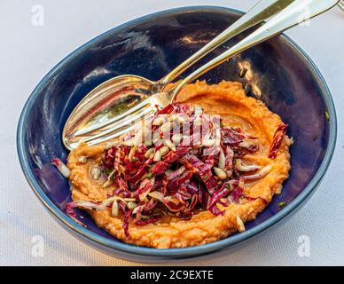 Un bol bleu foncé contient de la « Crema di Fagioli », une purée crémeuse de haricots géants, garnie d’une salade de radicchio et de graines de tournesol, avec une vaisselle en argent posée à côté. En 2020, pendant la pandémie de coronavirus, le restaurant La Cucina de l’hôtel Mühle à Binzen dans la région du Markgräflerland, en Bade-Wurtemberg, en Allemagne, est passé pour la première fois de sa cuisine markgräférienne aux plats apuliens. Banque D'Images