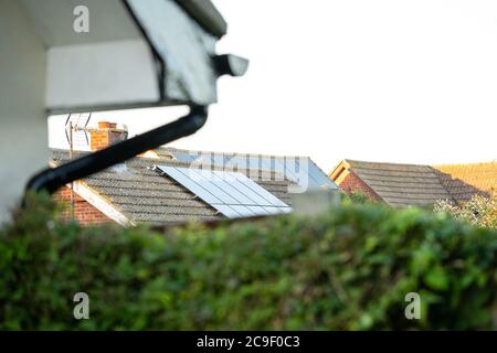 Panneaux solaires récemment installés vus sur le toit d'un bungalow, vu au-dessus d'une clôture de jardin et hedgerow. Banque D'Images